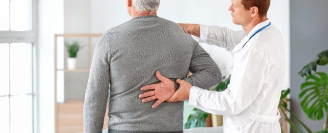 Doctor examining mature man with joint pain at home